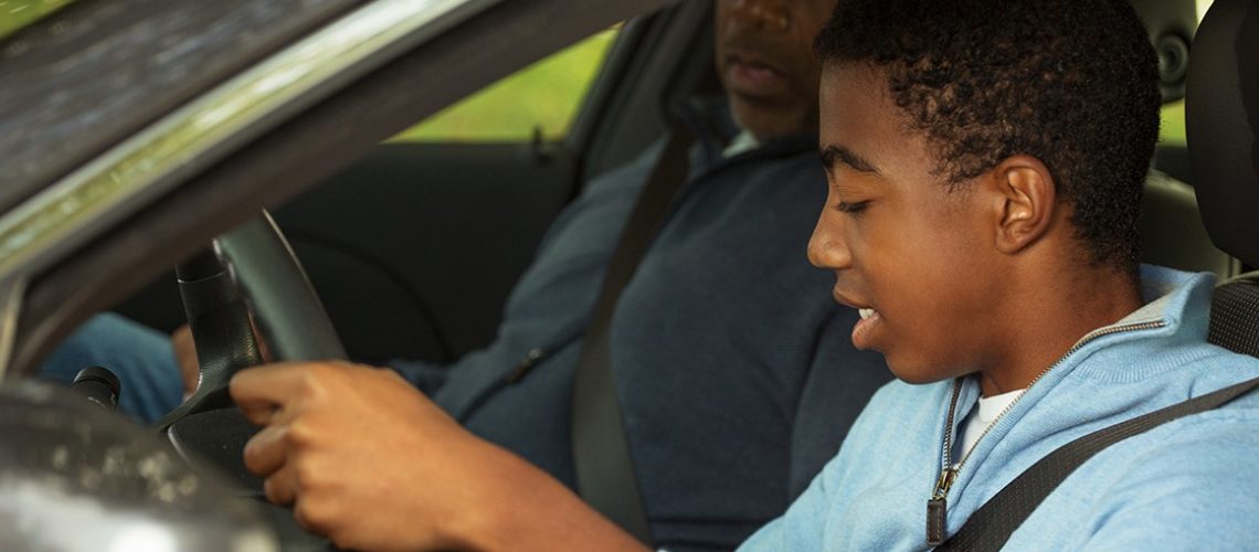 African American father teaching his son how to drive.